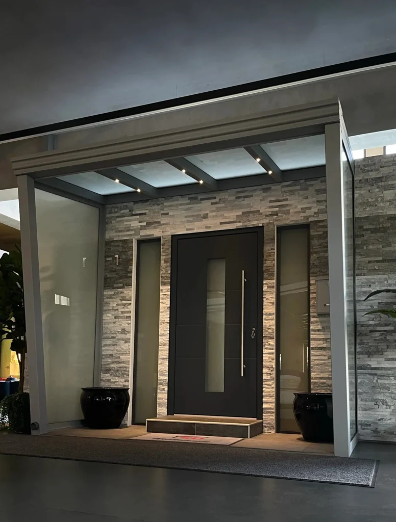 Eingangsportal Rösrath – Glasvordach mit LED-Spots, Glasseitenteilen und Naturstein-Wandverkleidung